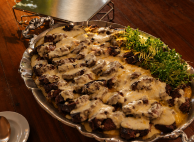 Travessa de prata com fatias de carne ao molho branco e brotos verdes