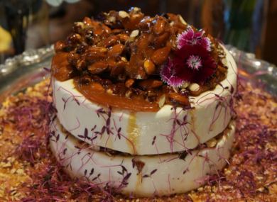 Queijos cremosos cobertos com nozes caramelizadas e flores roxas, em prato de prata